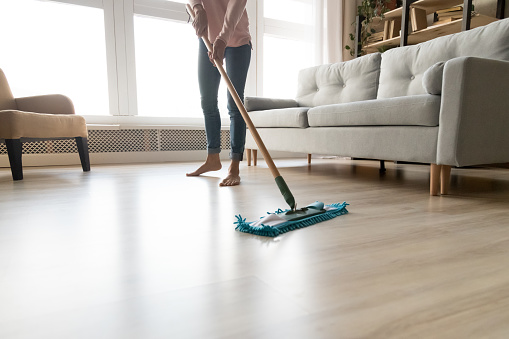 Cropped close up image of barefoot young woman in casual clothes washing heated wooden laminate warm floor using microfiber wet mop pad, doing homework cleaning routine, housekeeping job concept